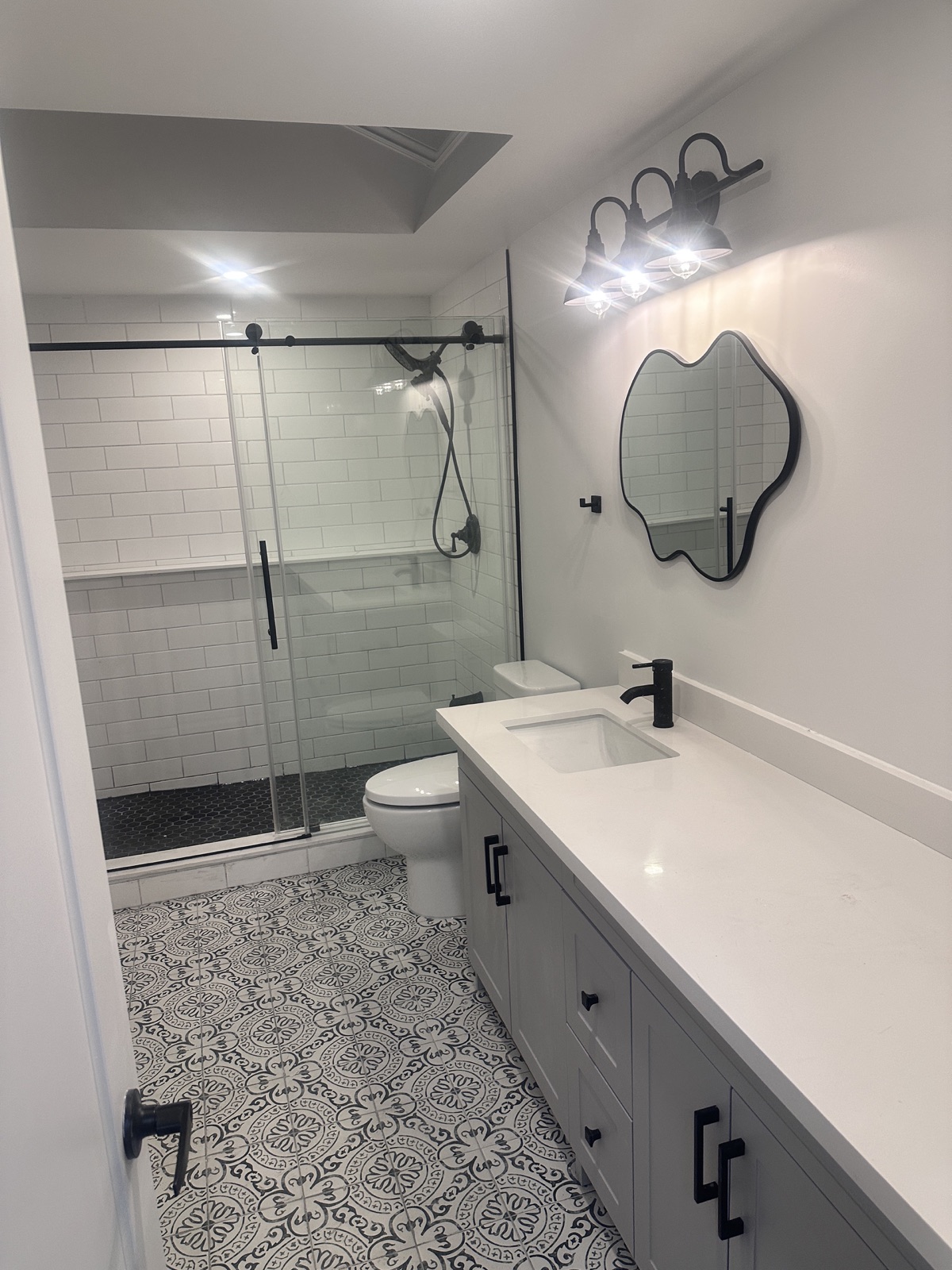 Bathroom after renovation with glass shower, vanity, patterned floor tile and black fixtures